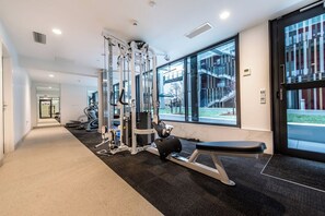 A gym with exercise equipment, a bench, and large windows offering a view of the outside. - Designed Penthouse 2Bed & 2Bath with SkyTower View on Queen St (Auckland)