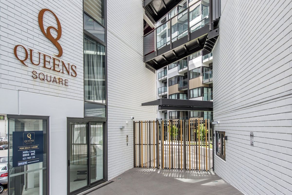 A modern building with a sign for 'Queens Square' and a gated entrance.