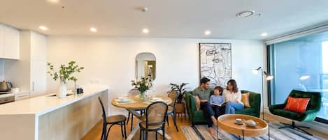 A modern living space with a dining area, a green sofa, and a large window.
