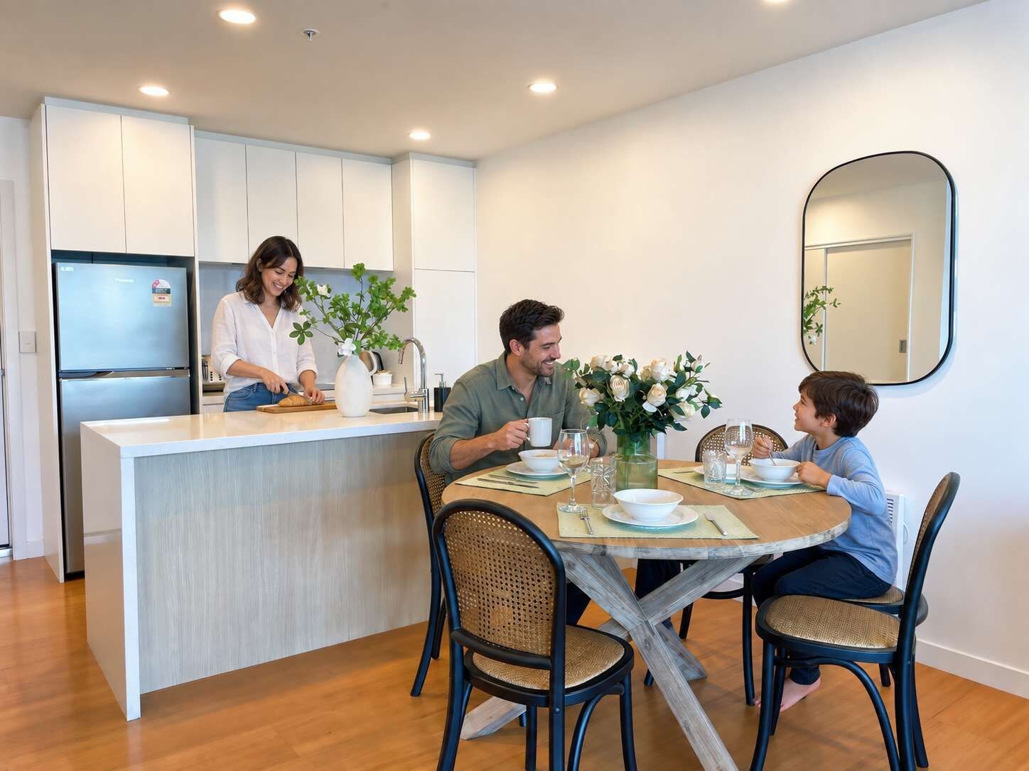 Una cucina moderna con mobili bianchi, un'isola centrale e un'area pranzo con tavolo in legno e sedie in vimini.