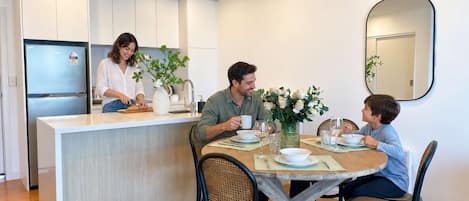A modern kitchen with white cabinets, a central island, and a dining area with a wooden table and wicker chairs.