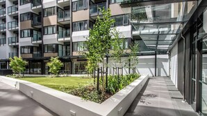 Um edifício moderno com várias varandas, fachada de vidro e um pátio ajardinado com árvores jovens.
