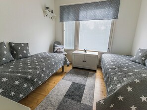 A bedroom with two beds, a nightstand, a dresser, and a window with blinds.