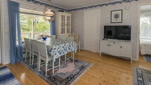 A dining area with a table set for four, a television on a cabinet, and a view of the outdoors through a window.