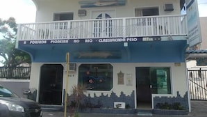 Un bâtiment à la façade bleue et blanche, sur lequel on peut lire l’inscription suivante : « A Pousada Pioneira no Rio – Établissement classé par le MTur ».