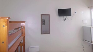 Une pièce avec un lit superposé en bois, des toilettes blanches, un téléviseur fixé au mur et une petite fenêtre.