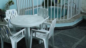 Un espace aménagé au bord de la piscine, avec une table ronde et des chaises en plastique blanc, le tout entouré d’une clôture en métal blanc.