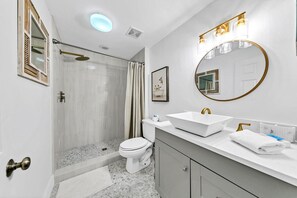 A modern bathroom with a shower, toilet, vanity, and a large mirror.