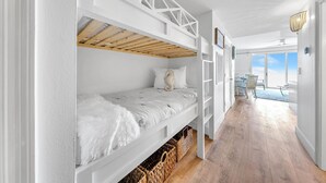 A bedroom with a bunk bed, wooden flooring, and a view to a balcony.