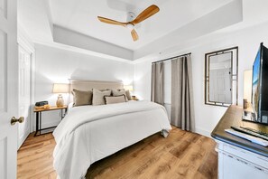 A bedroom with a bed, a ceiling fan, a TV, and a window with curtains.