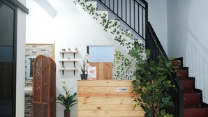 Eine Rezeption mit einem Schild, eine Treppe mit roten Stufen sowie eine Wand mit Regalen und Pflanzen.