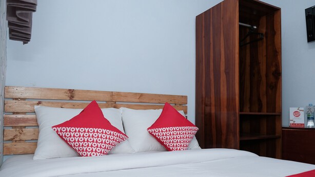 Ein ordentlich gemachtes Bett mit weißer und roter Bettwäsche, einem Holzkopfende und einem Kissen mit roten und weißen Mustern.