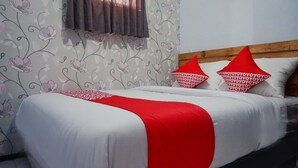 Ein ordentlich bezogenes Bett mit weißer und roter Bettwäsche, einem Holzkopfende und blumigem Wandpapier.