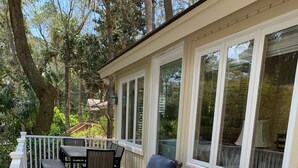 A covered outdoor deck with wicker furniture and a table, surrounded by white railings and large windows. - Private Home with SPA and Private pool, Beautiful Lagoon views (Hilton Head Island)