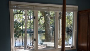 A room with a large window overlooking a lake, a wooden chair, and a bench by the water. - Private Home with SPA and Private pool, Beautiful Lagoon views (Hilton Head Island)