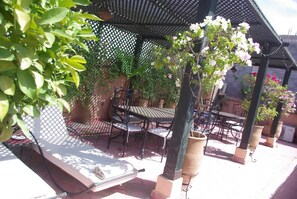 An outdoor patio with tables and chairs, surrounded by potted plants and a lattice structure overhead.