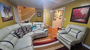 A living room with a sectional sofa, two armchairs, a staircase, and a hallway leading to another room.