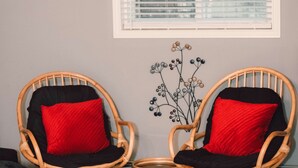 Two wicker chairs with red cushions and a small table, positioned in front of a window with blinds. - A Fisherman’s and birdwatchers Paradise! (Carrying Place)