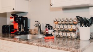 A kitchen with a granite countertop, a sink, a coffee maker, a spice rack, and a utensil holder. - A Fisherman’s and birdwatchers Paradise! (Carrying Place)