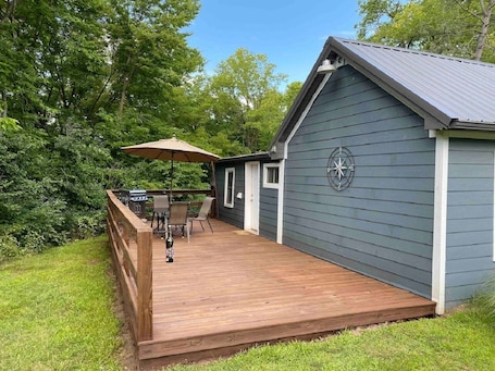 A deck with a grill and chairs, a covered area with an umbrella, and a compass on the building.