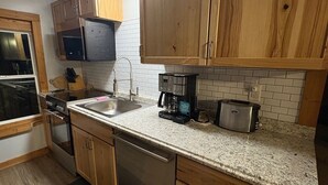 A compact kitchen with wooden cabinets, a stainless steel dishwasher, a microwave, a toaster, and a coffee maker.