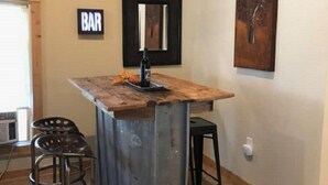 A bar area with a wooden counter, two stools, and a mirror on the wall.