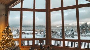 Tunnelmallinen huone, jossa on suuret ikkunat, puinen katto, joulukuusi ja kyltti, jossa lukee ”Lodge”.