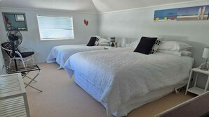 Ein Schlafzimmer mit zwei Betten, einem Ventilator, einem Sessel und einem kleinen Tisch.