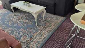 Ein Wohnzimmer mit einem schwarzen Sofa, roten und weißen Kissen, einem weißen Couchtisch und einem gemusterten Teppich.