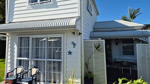 Ein zweistöckiges Haus mit überdachter Terrasse, einer kleinen Holzterrasse und einer sichtbaren Sitzgruppe im Freien.