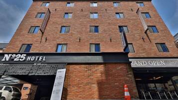 Um hotel com vários andares, fachada de tijolos, várias janelas e placas com a inscrição "No 25 Hotel" e "Grand Open".