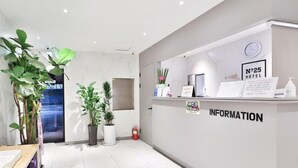 A hotel reception area with a reception desk, information sign, and potted plants. - NO25 (Incheon)