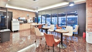 A modern cafe with marble flooring, white and orange chairs, and a kitchen area with a coffee machine. - NO25 (Incheon)