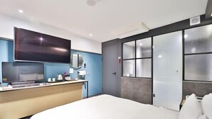 A modern hotel room with a large bed, a desk with a flat-screen TV, a mirror, and a large window with frosted glass panels. - NO25 (Incheon)