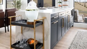 A modern kitchen with a large island, a black and gold cart with glasses, a white vase, and a clock on the wall. - Cottage with panoramic hilltop views and stocked pond on 80 acres.  (Spring Hill)