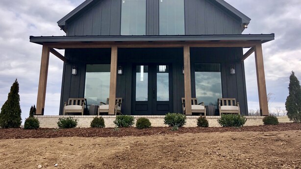 A two-story house with a covered porch, large windows, and a brick foundation. - Cottage with panoramic hilltop views and stocked pond on 80 acres.  (Spring Hill)