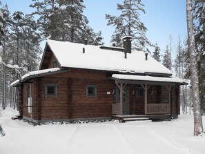 A wooden cabin with a snow-covered roof, surrounded by trees.
