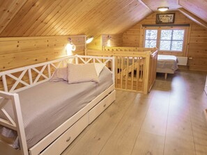 A cozy cabin with a loft-style bedroom featuring a bunk bed, a small desk, and a window with a view of snow-covered trees.
