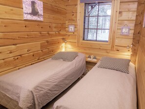 Une cabane avec deux lits, une fenêtre donnant sur une forêt enneigée et des murs en bois.