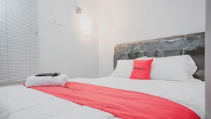 Une chambre d’hôtel avec un lit, une couverture rouge, un oreiller blanc et une serviette blanche posée sur le lit.