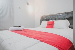 A hotel room with a bed, a red throw blanket, a white pillow, and a white towel on the bed. - Reddoorz Syariah Near Siloam Hospital Kebon Jeruk (Jakarta)