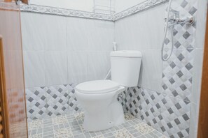 A bathroom with a toilet, a shower, and patterned tiles. - Reddoorz Syariah Near Siloam Hospital Kebon Jeruk (Jakarta)