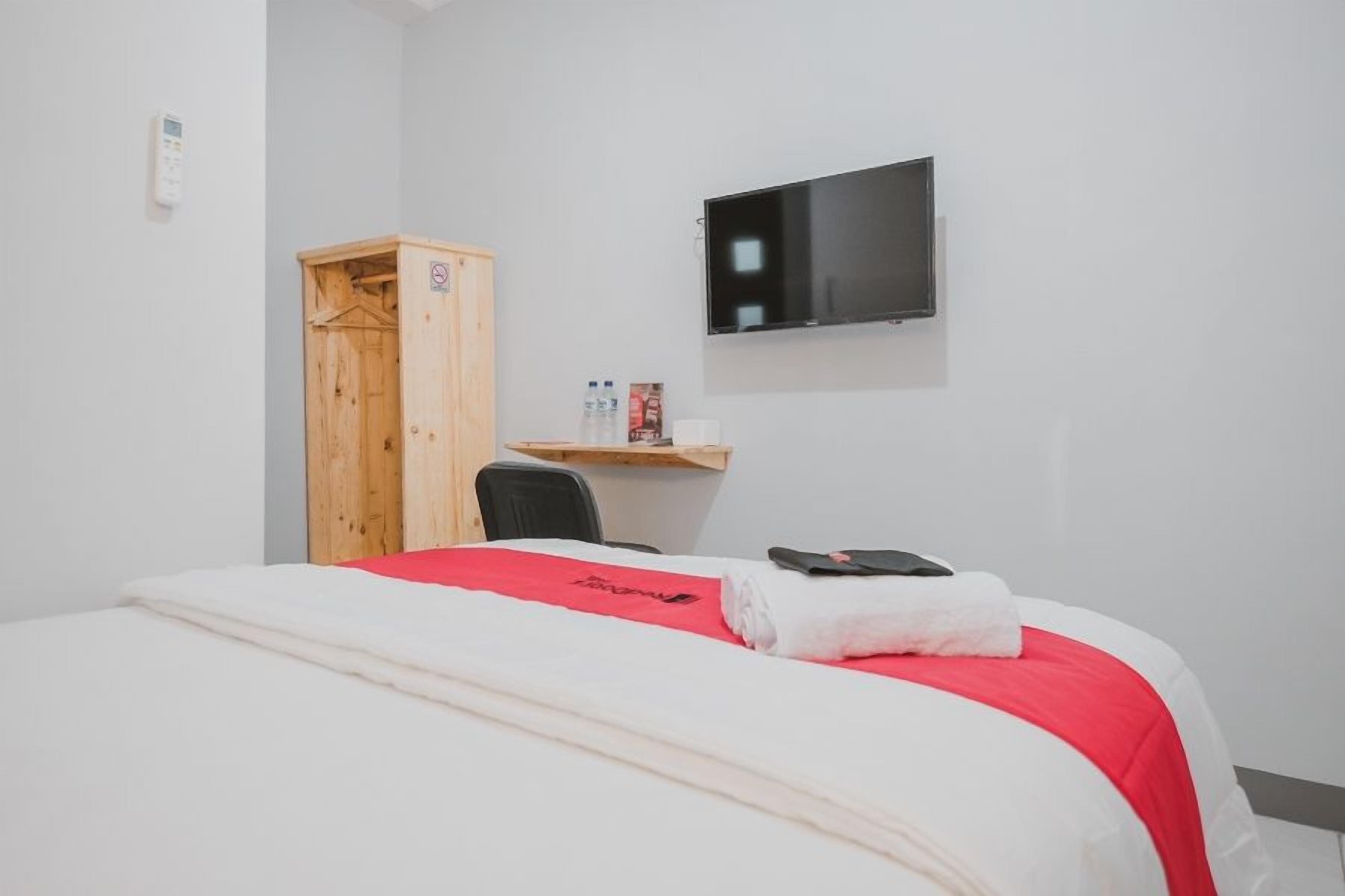 Une chambre d’hôtel comprenant un lit, une armoire en bois, une télévision et un petit bureau avec une chaise.