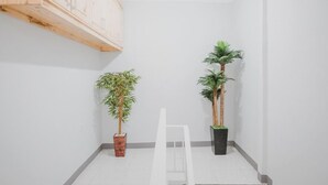 Um canto com uma cadeira branca, duas plantas em vasos e um armário de madeira.