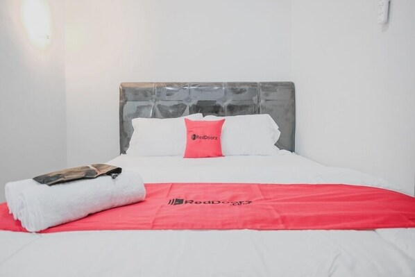 A neatly made bed with a red blanket and pillow, a white towel, and a small item on the bed.