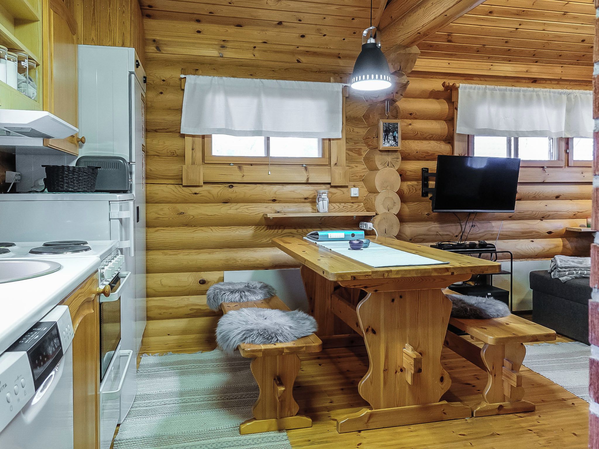 A cozy cabin interior with a wooden interior, a kitchen area with a stove and sink, a dining table, and a television mounted on the wall.