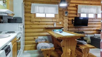 A cozy cabin interior with a wooden interior, a kitchen area with a stove and sink, a dining table, and a television mounted on the wall.