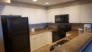 A kitchen with white cabinets, a black refrigerator, a microwave, a stove, and granite countertops.
