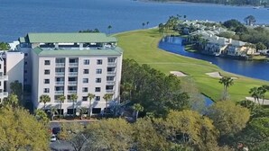 A multi-story hotel with a green roof, situated near a golf course and a body of water.