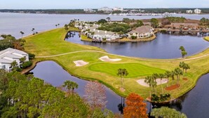 A golf course with a water body, surrounded by trees and buildings.